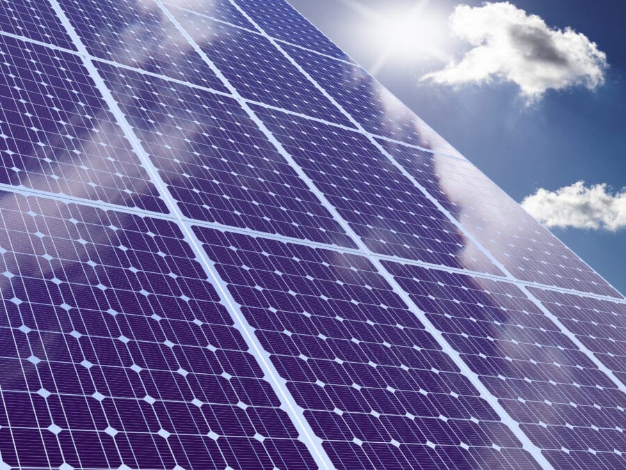 Blue solar panel with clouds and sun flare in background