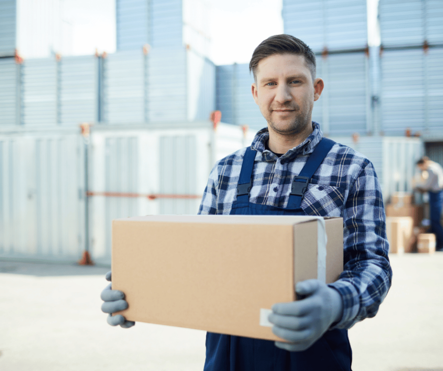 A man holding a box outside of multiple storage containers